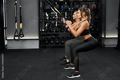 Girlfriends doing squatting with trx system.