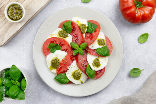 Traditional italian caprese salad with sliced tomatoes, mozzarella, basil, pesto sauce and spice on a light background. Top view.