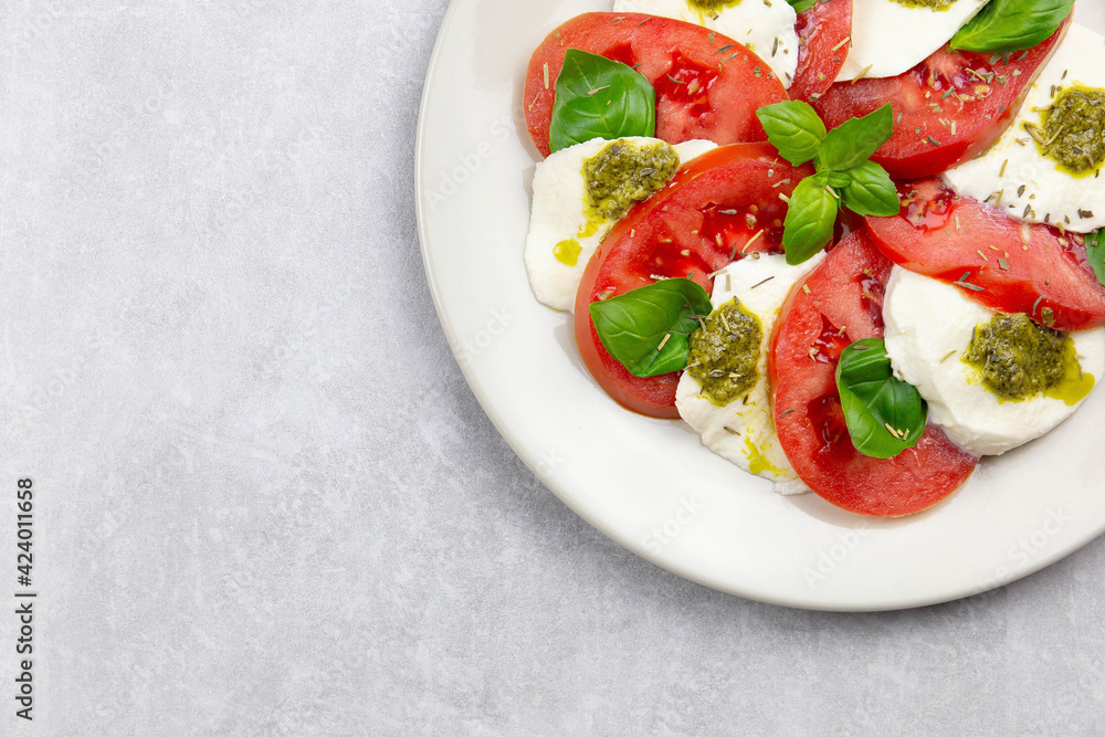Traditional italian caprese salad with sliced tomatoes, mozzarella, basil, pesto sauce and spice on a light background. Top view. Copy space. Close up. Traditional italian caprese salad with sliced tomatoes, mozzarella, basil, pesto sauce and spice on a light background. Top view. Copy space. Close up.