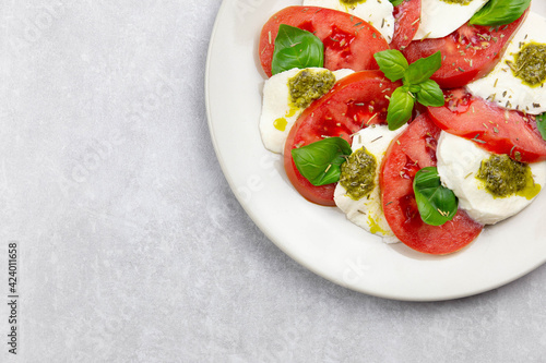 Traditional italian caprese salad with sliced tomatoes, mozzarella, basil, pesto sauce and spice on a light background. Top view. Copy space. Close up.