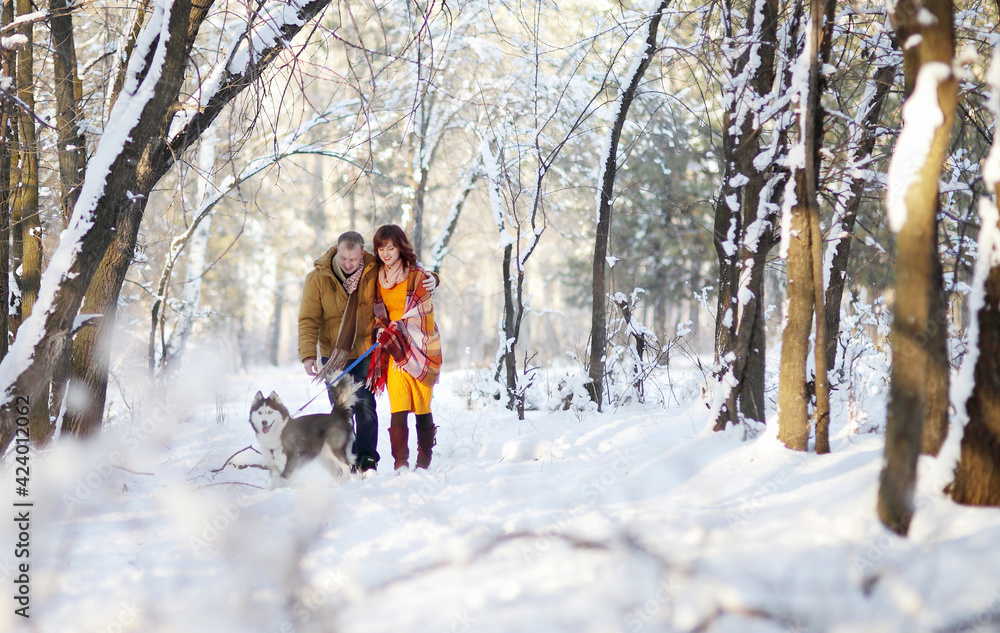 Naklejka premium Young couple smiling and having fun in winter park with their husky dog