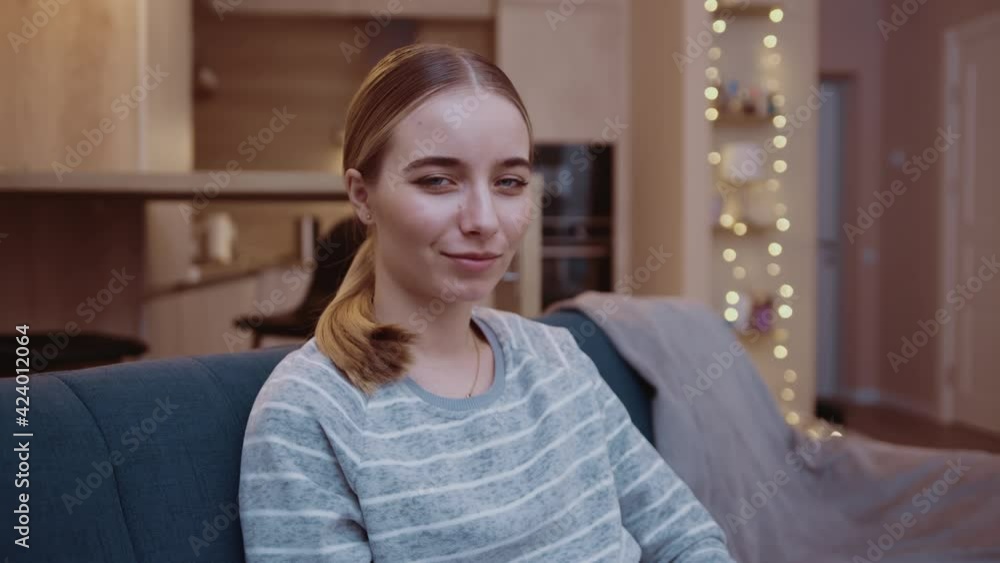 Cute face young woman look at camera sitting on sofa smiling feel happy. Confident, enjoying, joyful, relaxed, indoors, beauty, feminine, female, adult, attractive. Slow motion Cute face young woman look at camera sitting on sofa smiling feel happy. Confident, enjoying, joyful, relaxed, indoors, beauty, feminine, female, adult, attractive. Slow motion