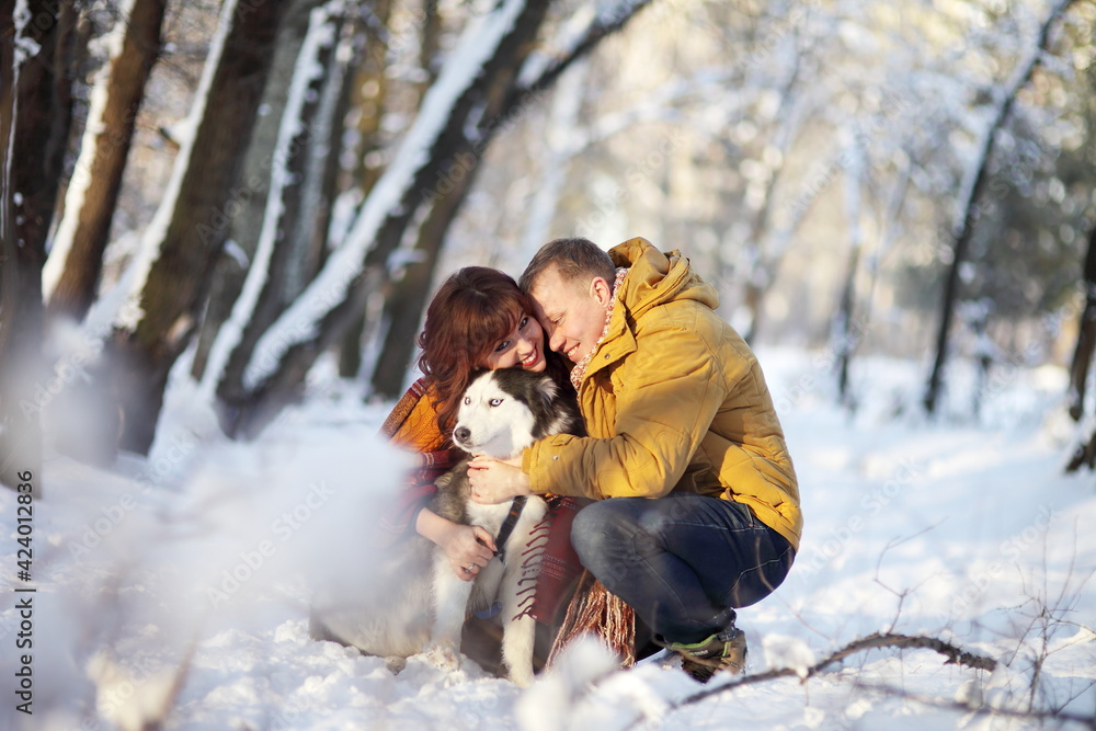 Couple smiling and having fun in winter park with their husky dog Couple smiling and having fun in winter park with their husky dog