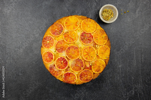 Upside down blood orange and polenta cake with pistachio nut on dark background. Homemade cake with citrus fruits. Top view.