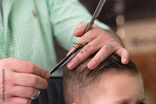 Barber in barbershop cuts hair happy child boy. Lifestyle close-up. Concept of beauty, hygiene and care salon