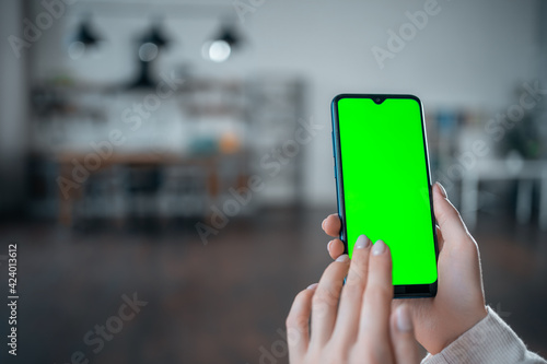 closeup of female hand using or clicking smartphone with green screen at home