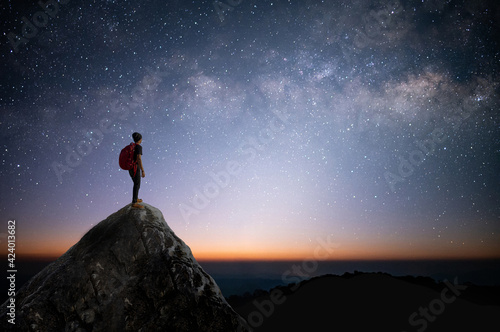 Silhouette of young traveler and backpacker standing on the rock watched the star and milky way. He enjoyed traveling and was successful when he reached the summit.