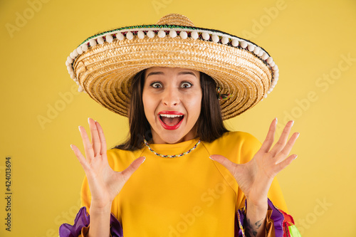 Young beautiful girl in sombrero isolated over yellow background.