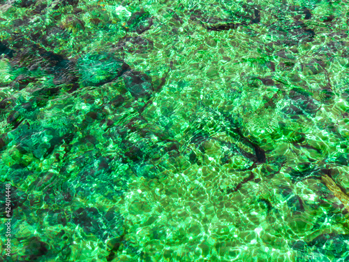 Transparent waves of the green river with stones under in the water and sunlight water reflection