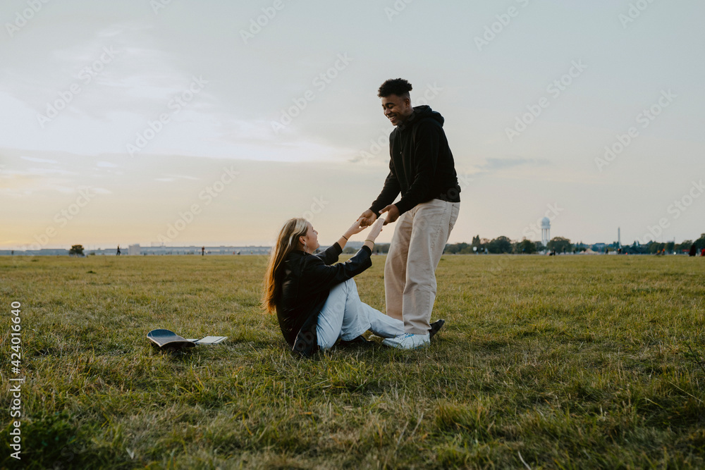 Smiling man holding hands of female friend sitting in park Smiling man holding hands of female friend sitting in park