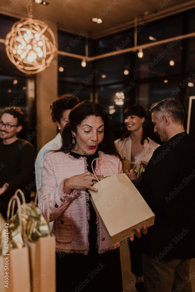 Surprised female entrepreneur peeking in gift bag during party in office Surprised female entrepreneur peeking in gift bag during party in office