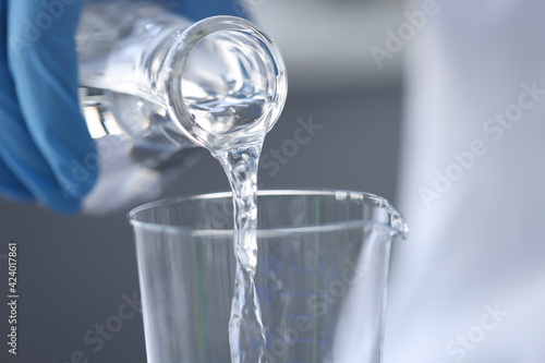 Scientist chemist in gloves pouring water from flask into glass closeup photo