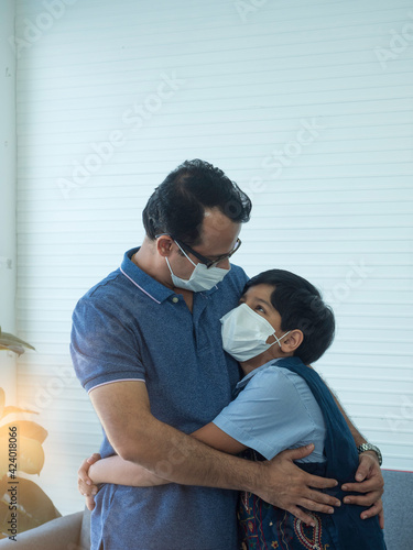 Indian dad and son wearing medical mask, hugging each other. New Normal lifestyle during outbreak of Coronavirus or Covid-19.