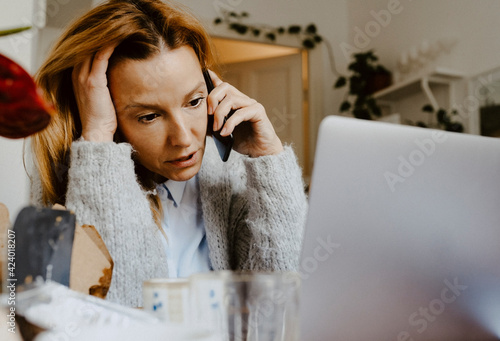 Mature businesswoman with hand in hair talking on smart phone at home photo