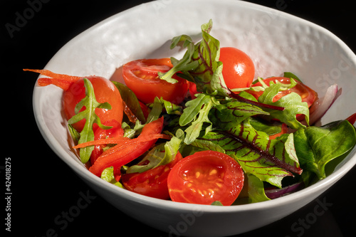 Vegetarian salad of cherry tomatoes, spinach, red onions and bell peppers with butter. On a black background.