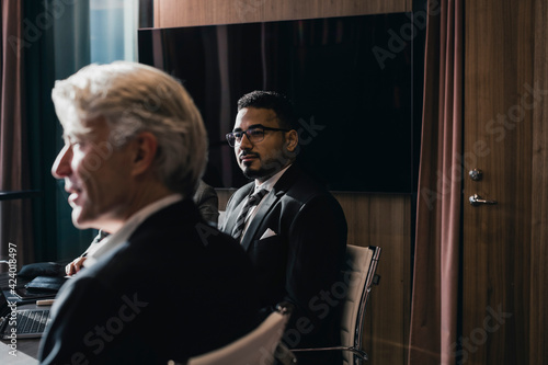 Confident businessman sitting with senior male colleague in board room during meeting