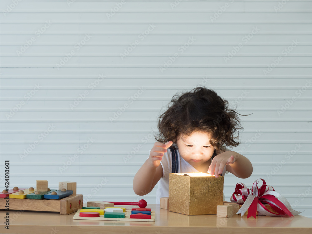 Cute little toddler girl with messy hairstyle looking at bright light in gift box with curiousity on the face. Cute little toddler girl with messy hairstyle looking at bright light in gift box with curiousity on the face.