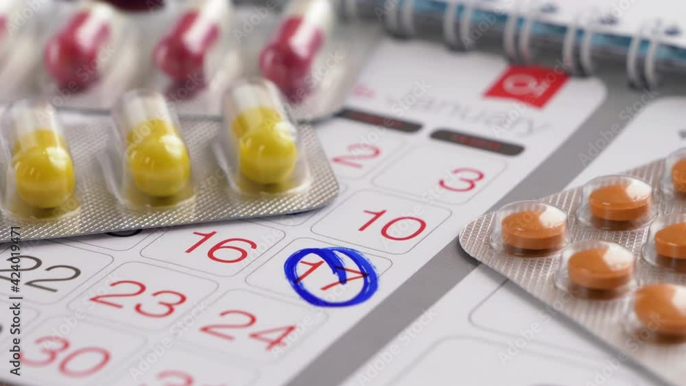 Mark on paper calendar or schedule. Pills in a blister pack and capsules lie near the calendar. Hand with a pen mark on a calendar date. Treatment and medications, doctor's visit concept. Mark on paper calendar or schedule. Pills in a blister pack and capsules lie near the calendar. Hand with a pen mark on a calendar date. Treatment and medications, doctor's visit concept.