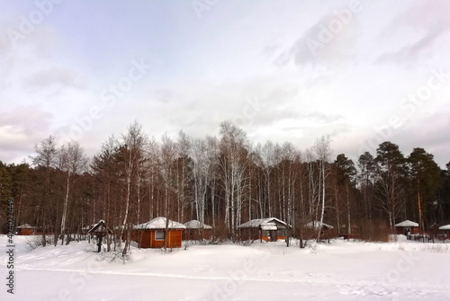 Wood houses beside the lake in pine forest. A cottages in the middle of the frozen forest at winter.  © Elena