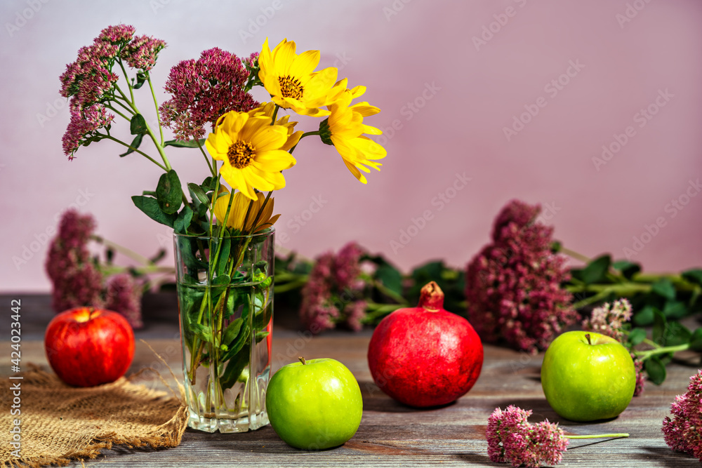 Bouquet of flowers in a vase next to apples and pomegranate on a wooden table Bouquet of flowers in a vase next to apples and pomegranate on a wooden table