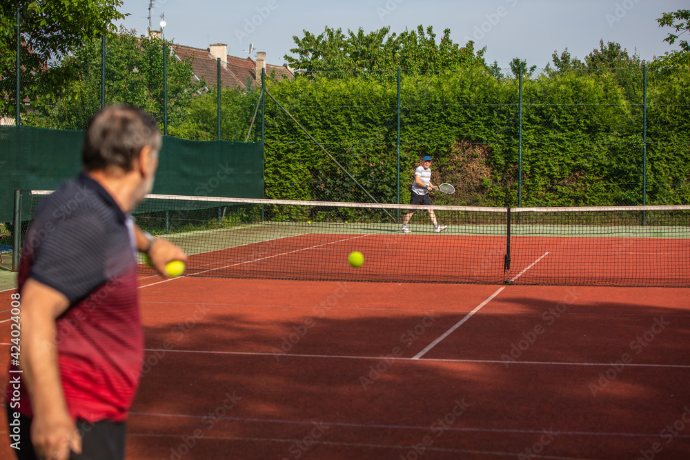 Pensioners playing tennis outside on the clay tennis court, active seniors, sport concept