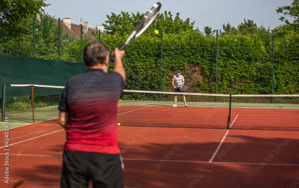Pensioners playing tennis outside on the clay tennis court, active seniors, sport concept