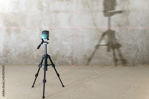 The laser level projects red lines onto the wall with a rough finish