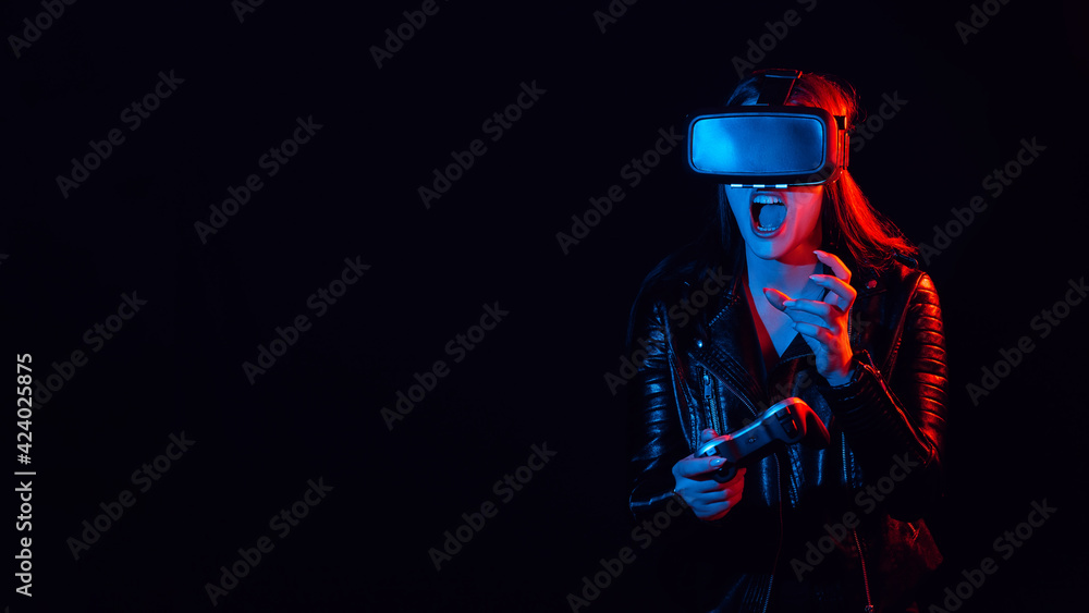 Girl plays modern computer games in virtual reality glasses. Emotional gamer with a joystick in his hands is immersed in world of augmented reality Girl plays modern computer games in virtual reality glasses. Emotional gamer with a joystick in his hands is immersed in world of augmented reality