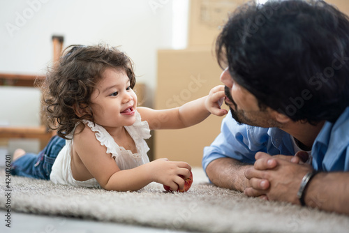 Cute little girl using finger touch her father mouth while lying on floor in living room, Happy family concept