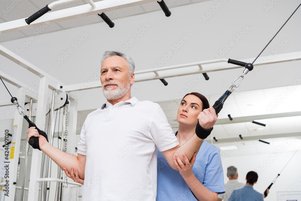trainer supporting mature man training on pull rope exercising machine trainer supporting mature man training on pull rope exercising machine