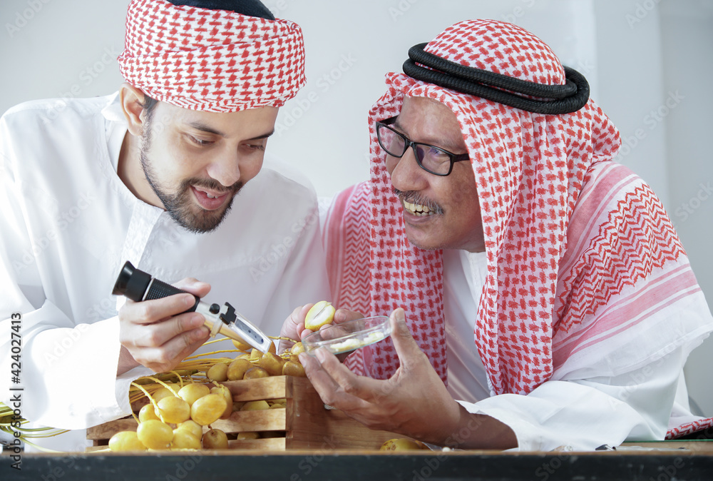 Arab senior and young man smiling and holding Brix Refractometer and glass plate contain piece of date palm slices for test sweetness level of sugar in fruits
