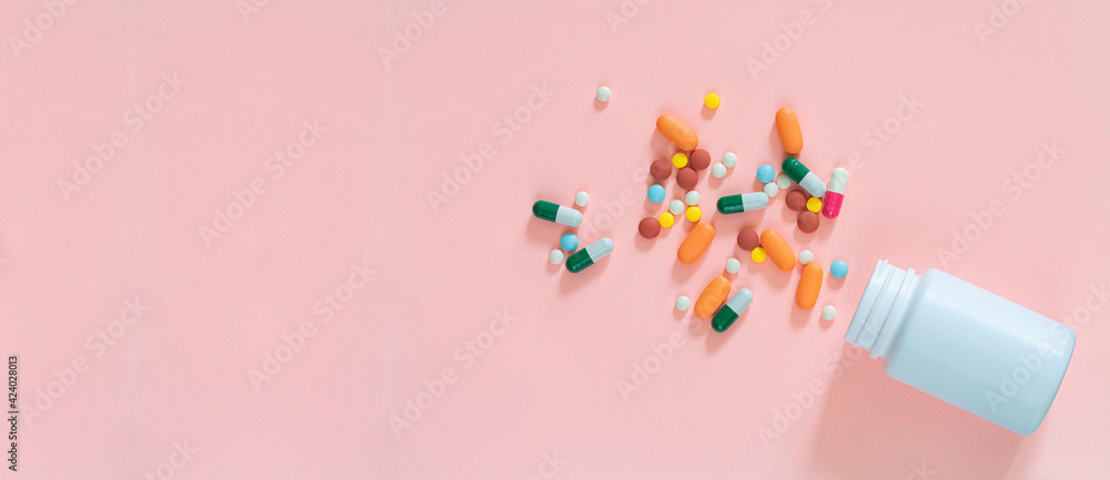Multicolored tablets, pills, capsules in plastic bottle on pink background, copy space. Medicine, vitamin and nutritional supplements concept. Multicolored tablets, pills, capsules in plastic bottle on pink background, copy space. Medicine, vitamin and nutritional supplements concept.