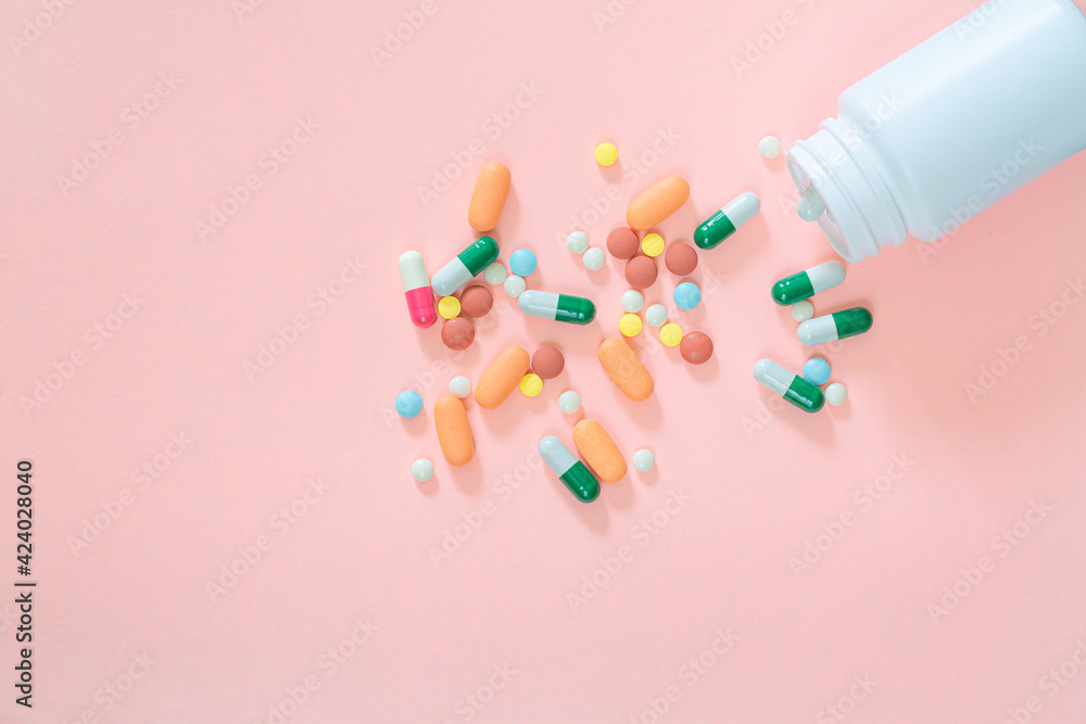 Multicolored tablets, pills, capsules in plastic bottle on pink background, copy space. Medicine, vitamin and nutritional supplements concept. Multicolored tablets, pills, capsules in plastic bottle on pink background, copy space. Medicine, vitamin and nutritional supplements concept.