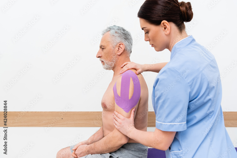 physiotherapist applying kinesio tape on shoulder of mature man physiotherapist applying kinesio tape on shoulder of mature man