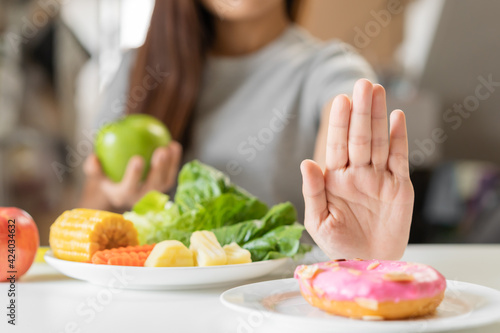 Diet  Dieting young asian woman or girl use hand push out  deny sweet donut and choose green apple  vegetables salad  eat food for good healthy  health when hungry. Close up female weight loss person.