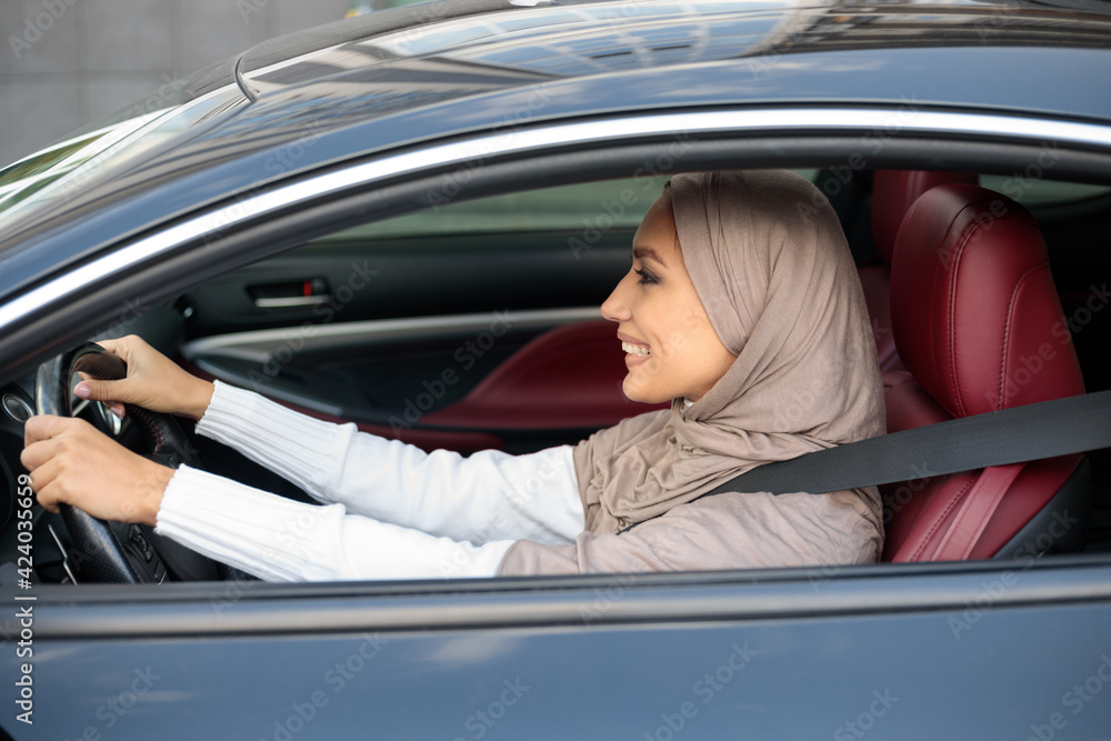 Cheerful happy muslim woman in hijab driving her new car