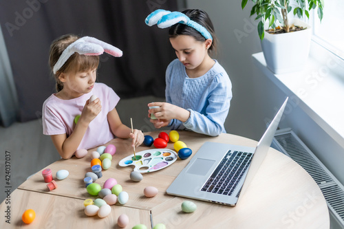 Two little cute girls with bunny ears are painting Easter eggs, children are preparing for the spring holiday, Easter mood, children are drawing on eggs.