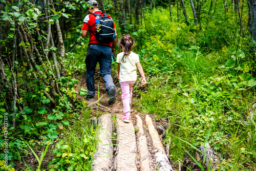 Father and daughter go camping in the woods. Tourism with children. Walking in the woods with a girl and a father. Father and daughter cross wooden bridge