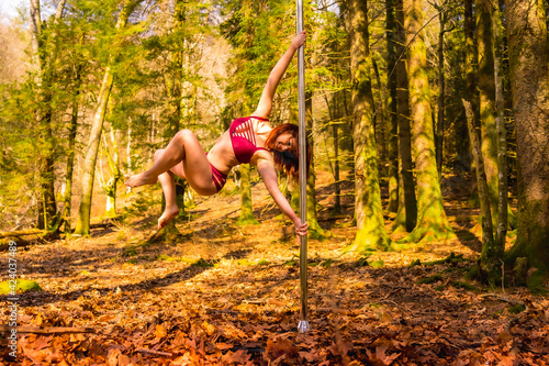 Exercises of a Caucasian acrobat dancing pole dance in the forest in autumn. Circus stunts in nature photo