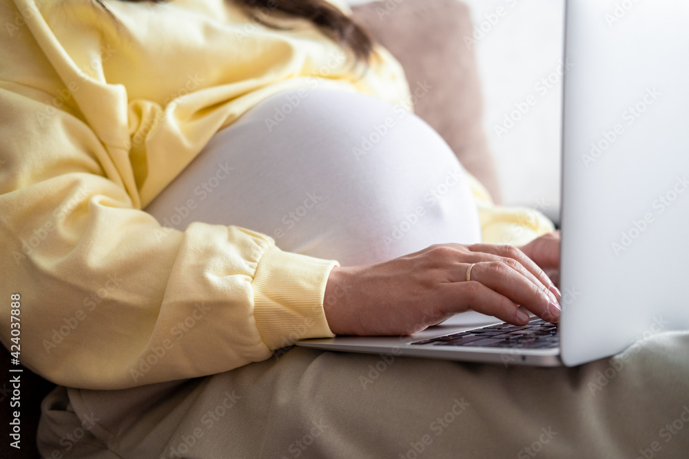 Naklejka premium Attractive pregnant young lady working remotely online from home. Close up woman hands on laptop with big belly advanced pregnancy.