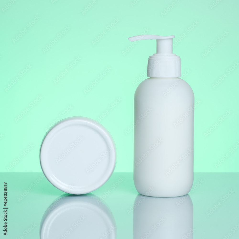 Hand cream in a bottle and jar on a mint background with reflection. Hand cream in a bottle and jar on a mint background with reflection.