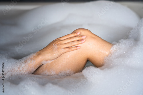 Action of woman hand is patting on the leg for clean skin during taking spa massage in foaming bathtub. Healthcare  skincare and beauty relaxation activity concept photo.