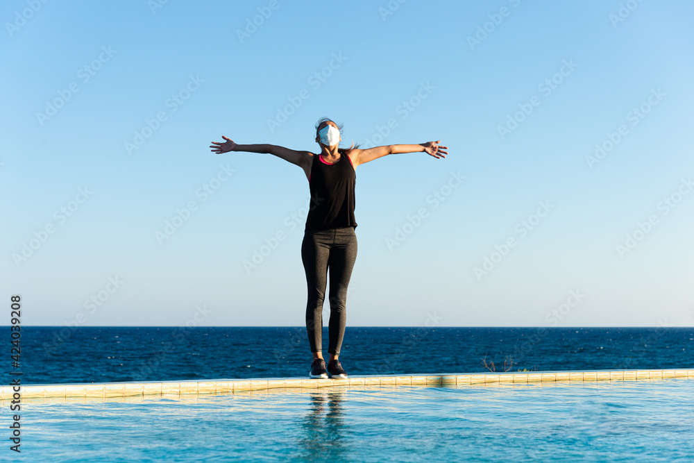 Young woman with protective surgical face mask performing yoga stretching exercises outdoor during covid-19 coronavirus pandemic Young woman with protective surgical face mask performing yoga stretching exercises outdoor during covid-19 coronavirus pandemic
