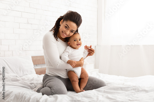 Young Black Mom Posing Holding Baby Toddler Sitting In Bedroom