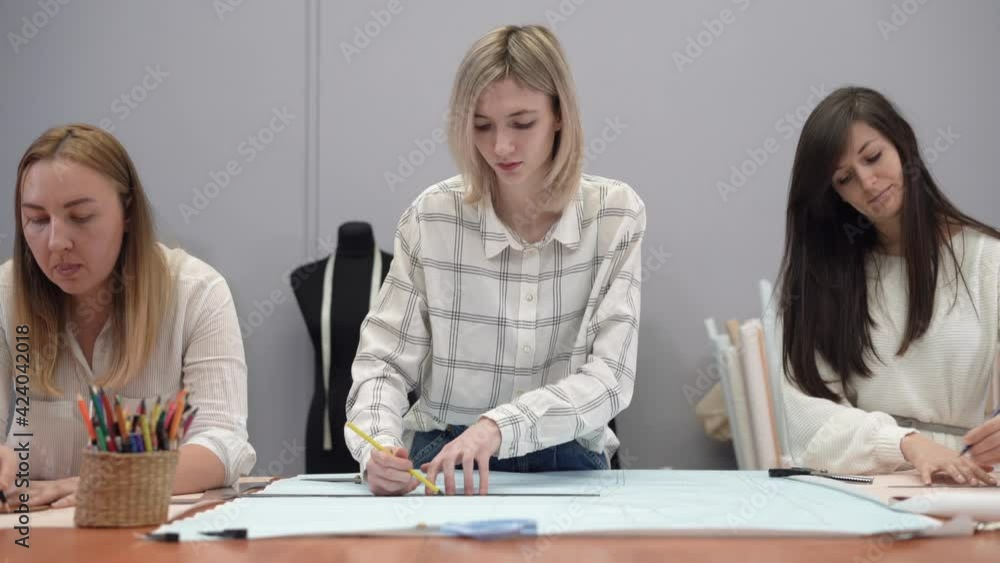 master draws a sketch of a collection of clothes on paper. Two Caucasian women fashion designers draw a sketch on graph paper. master draws a sketch of a collection of clothes on paper. Two Caucasian women fashion designers draw a sketch on graph paper.
