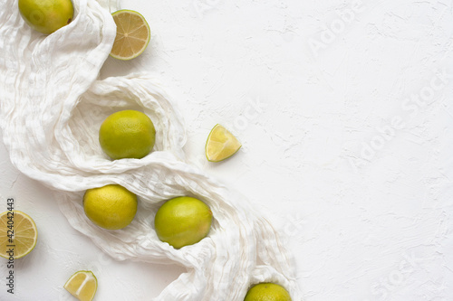 Raw limes on tablecloth and a white textural background.
