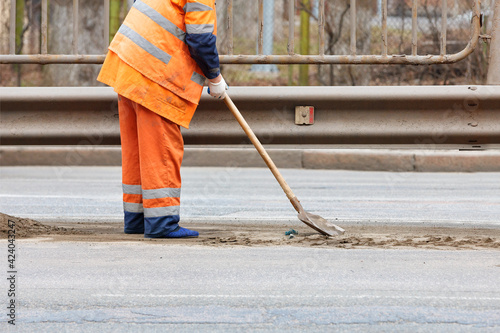A road service worker uses a shovel to scrape off accumulated sand and debris between the lanes of the road.