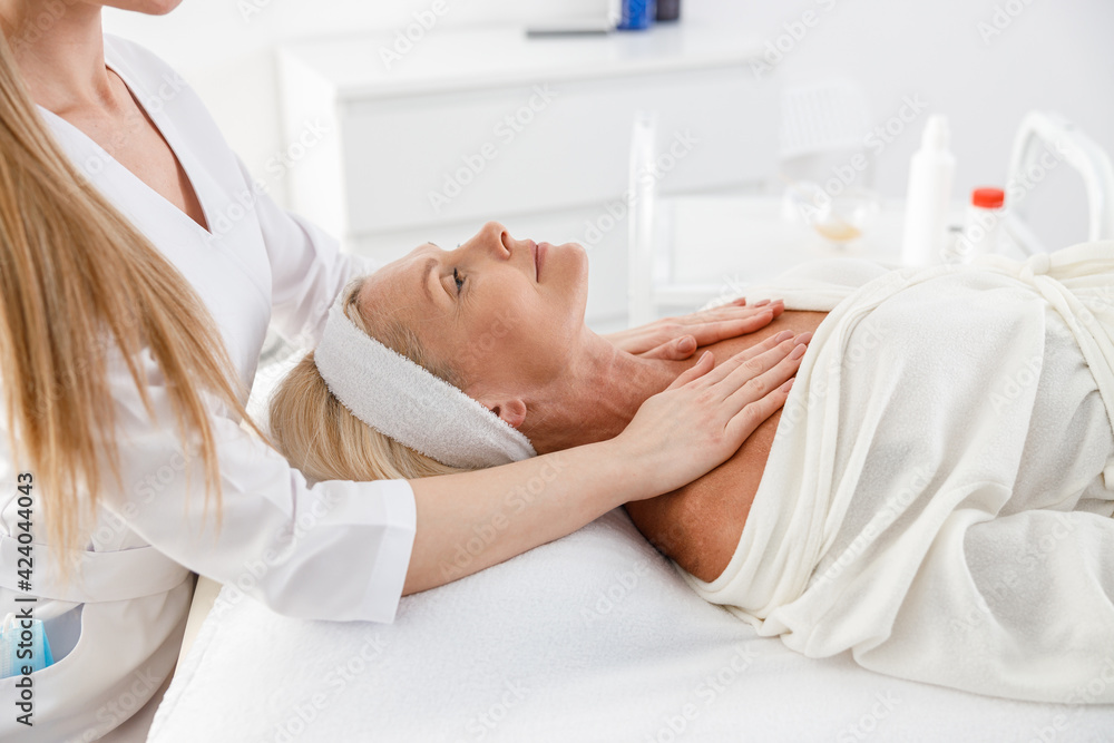 Senior female is lying on back, getting face lifting massage. Facial massage beauty treatment. Wellness, beauty and relaxation concept Senior female is lying on back, getting face lifting massage. Facial massage beauty treatment. Wellness, beauty and relaxation concept