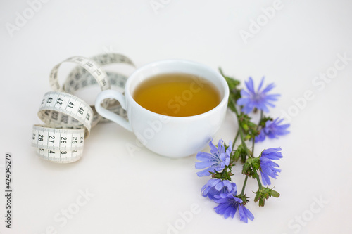 Cup with herbal tea and measuring tape on a white background. Weight loss concept.