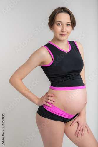 Young adult pregnant girl in sportswear. Sport and pregnancy concept. Yoga and fitness in anticipation of childbirth. White background.